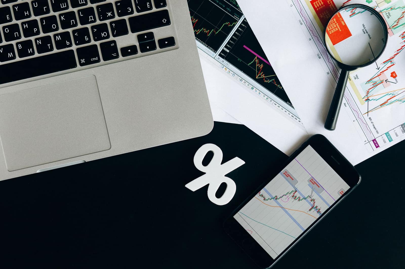Overhead view of financial charts, a laptop and a smartphone laid out on a desk