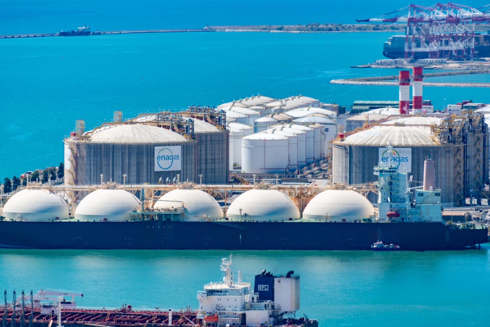Aerial view of an LNG terminal with storage tanks and tanker ships docked at a coastal port