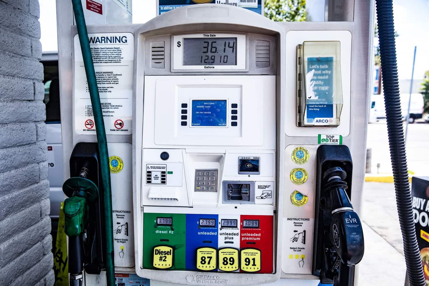 A fuel dispenser nozzle resting in its holder at a petrol station forecourt