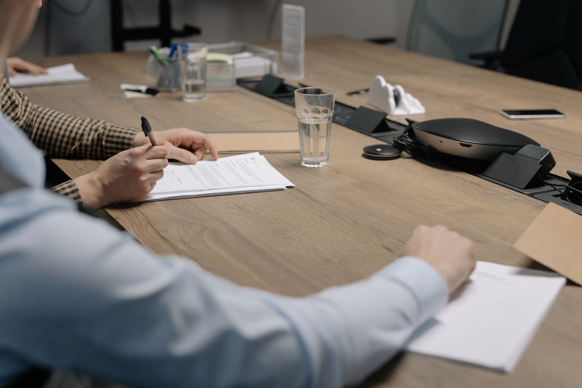 Two professionals signing documents across a table in an office meeting