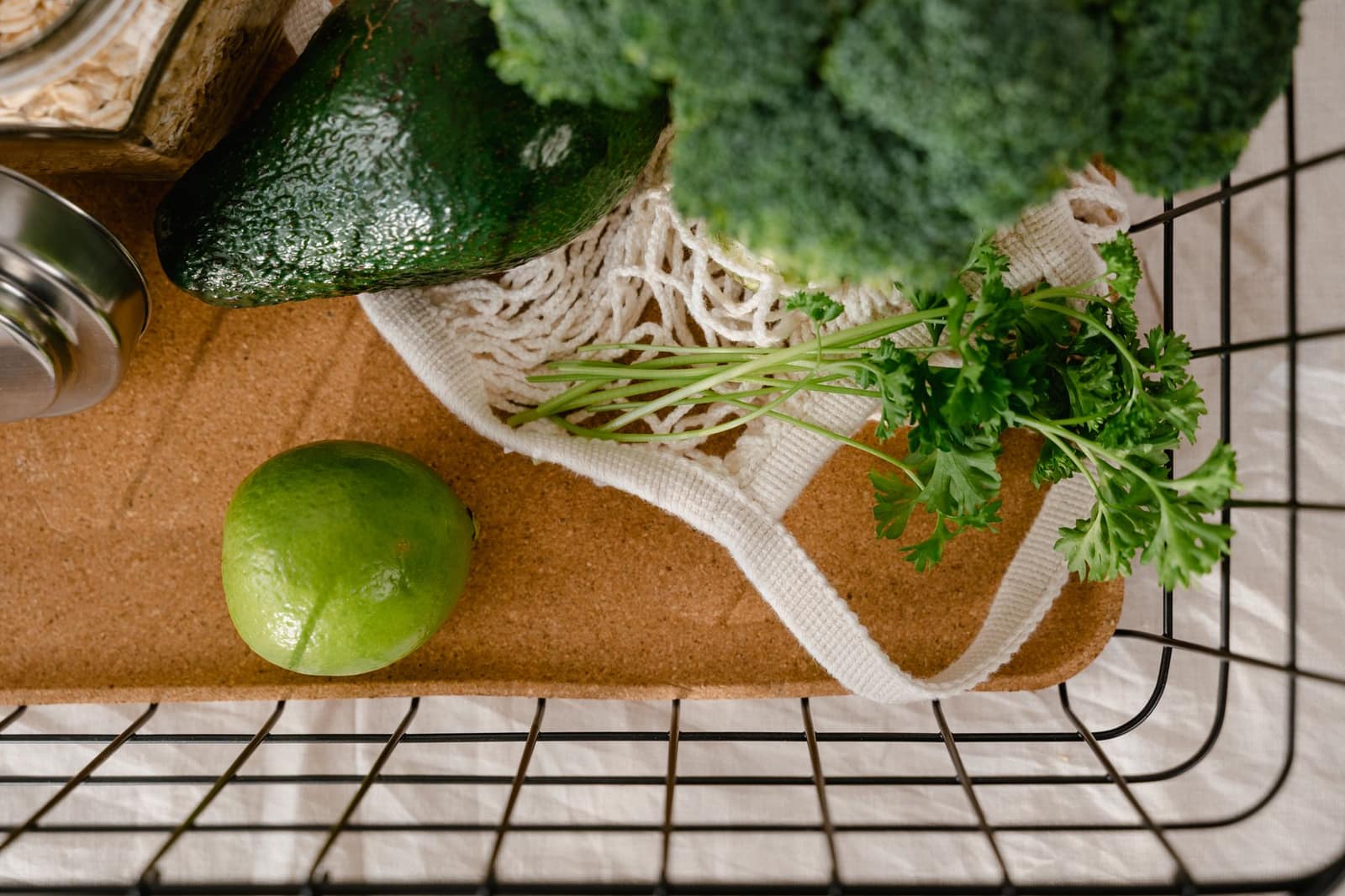 An avocado, lime and fresh greens in a reusable mesh shopping bag on a kitchen counter