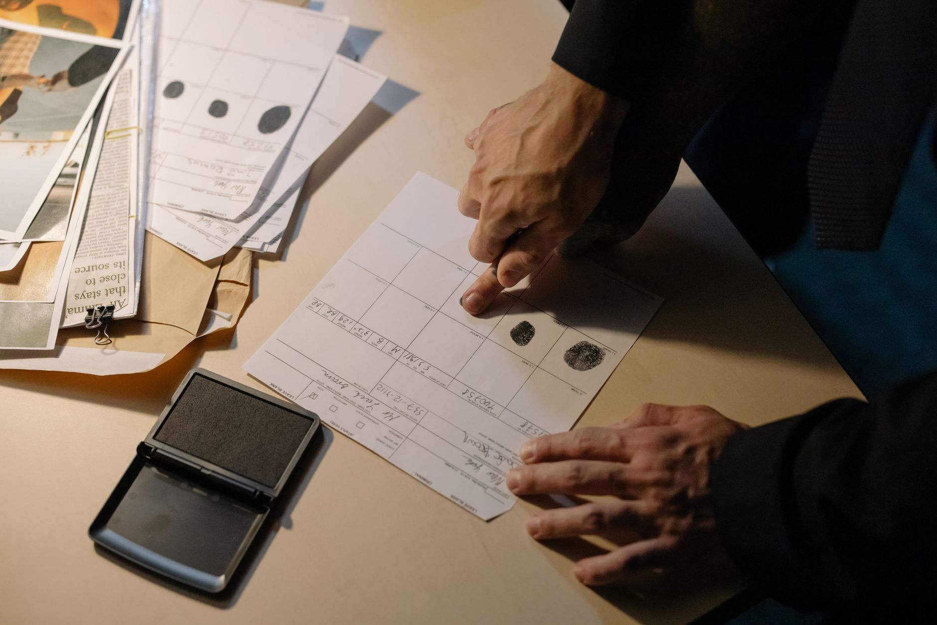 A person's hand pressing a fingerprint onto paper on a desk with an ink pad