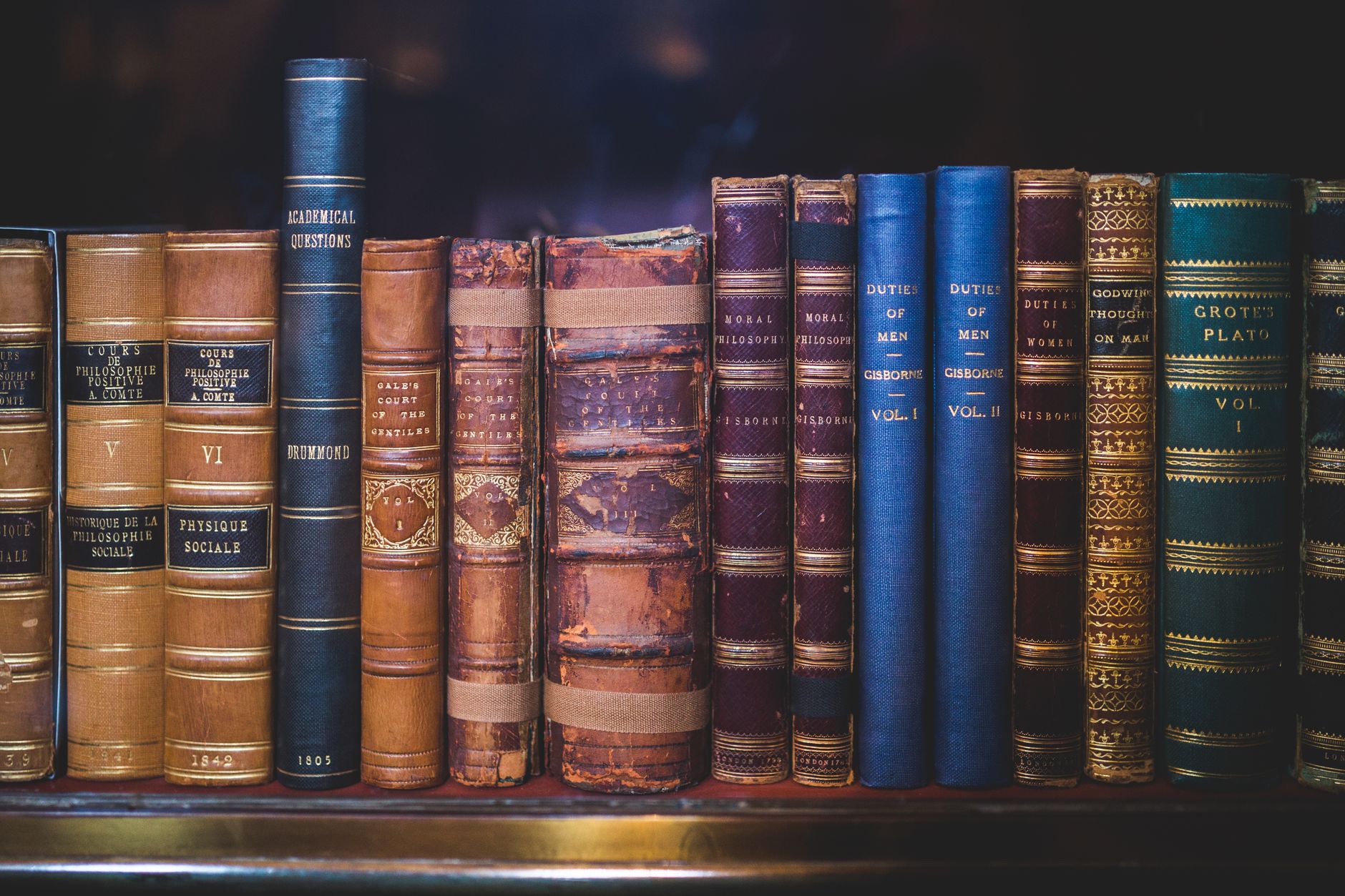 A collection of classic, leather-bound books arranged on a wooden bookshelf