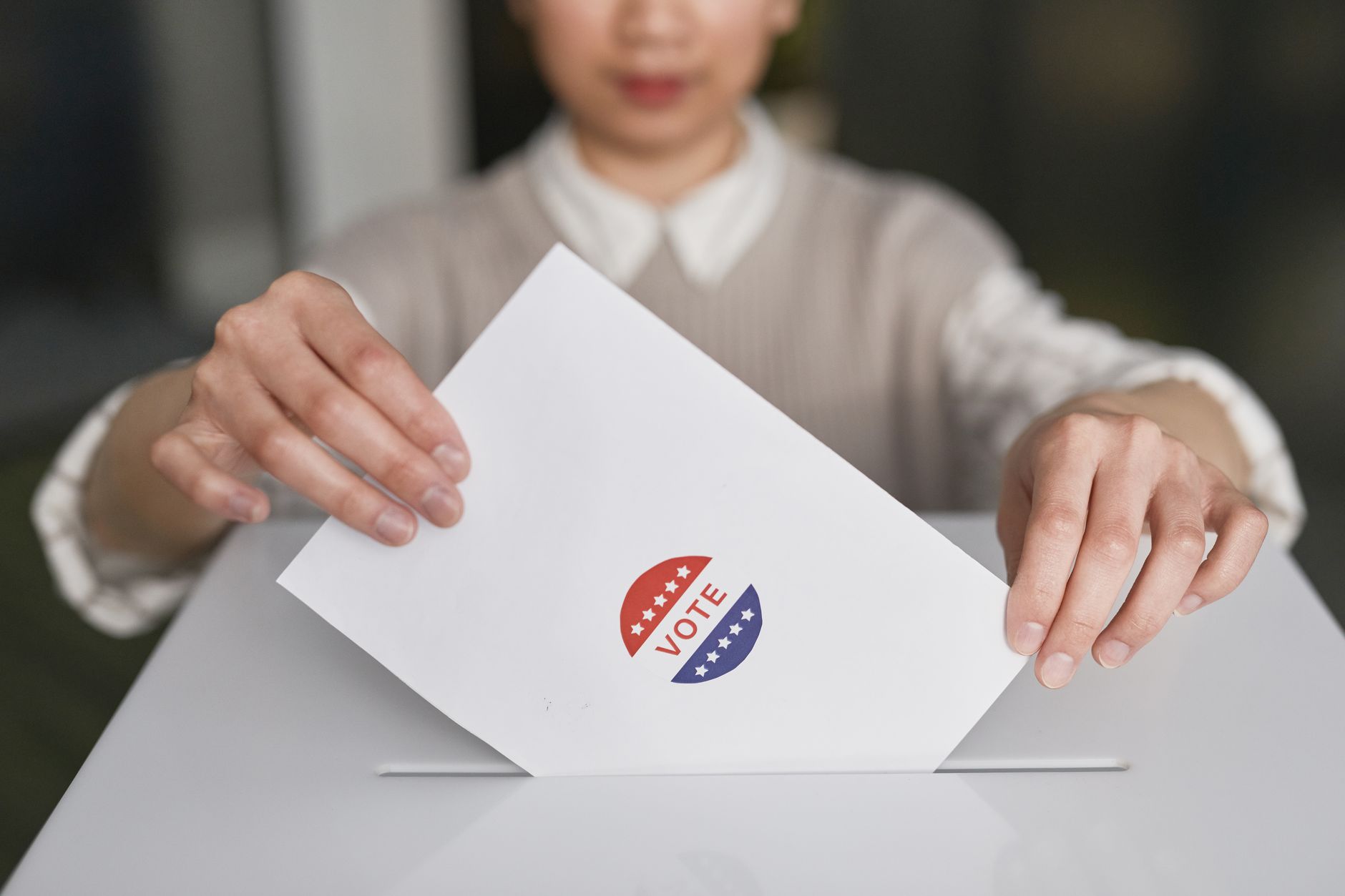 A person casting a paper ballot into a ballot box