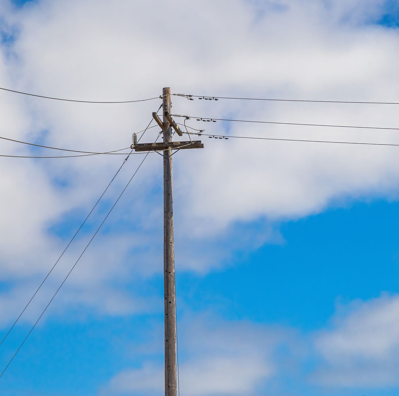 Wooden power pole with electricity transmission lines against a clear sky