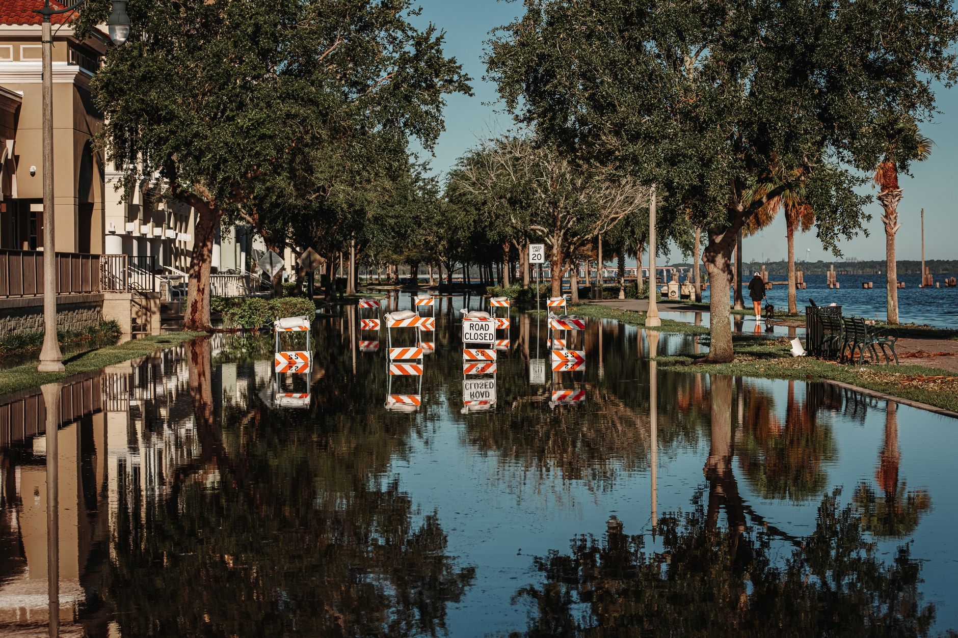 A flooded street with road-closed signs reflected in the water