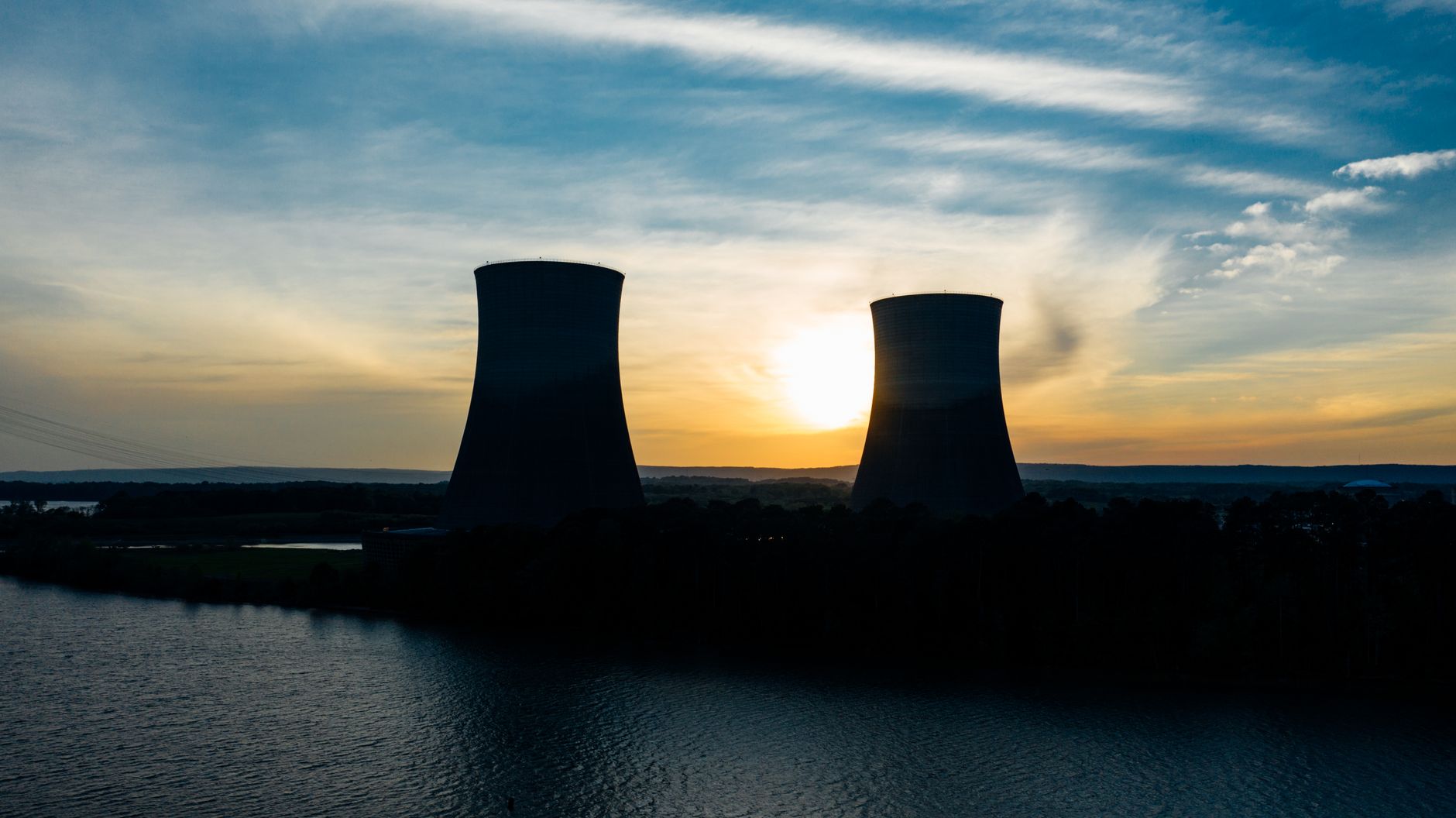 Cooling towers at a nuclear power plant silhouetted against a cloudy sky at sundown