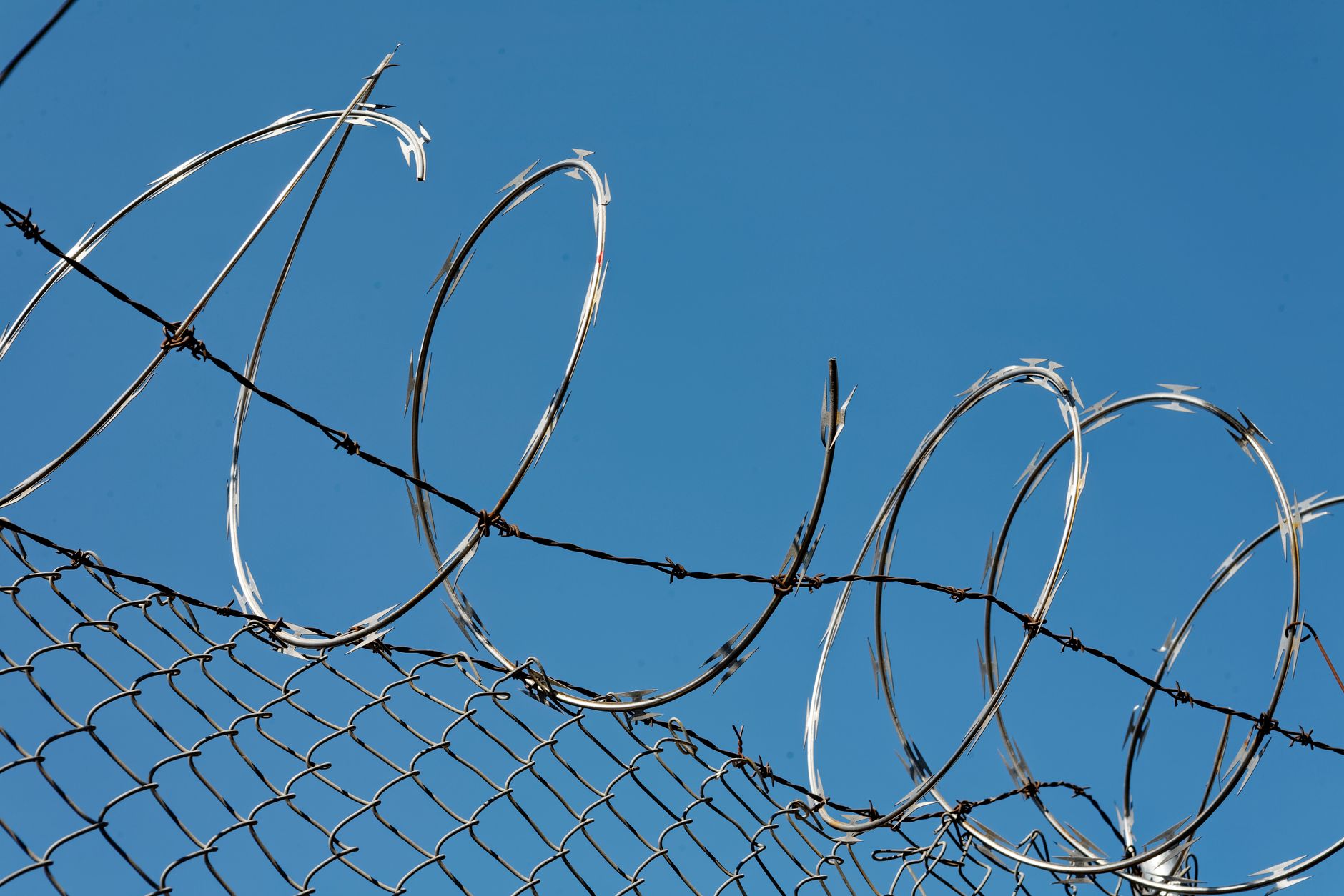 Close-up of razor wire on a chain-link fence against a clear blue sky