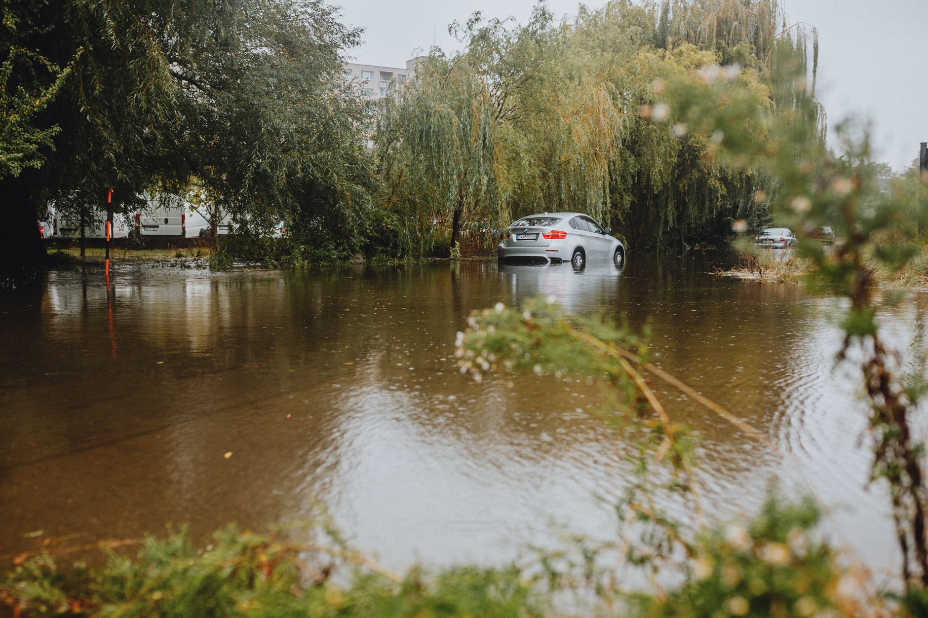 A car struggles through a flooded street surrounded by trees after a heavy rainstorm