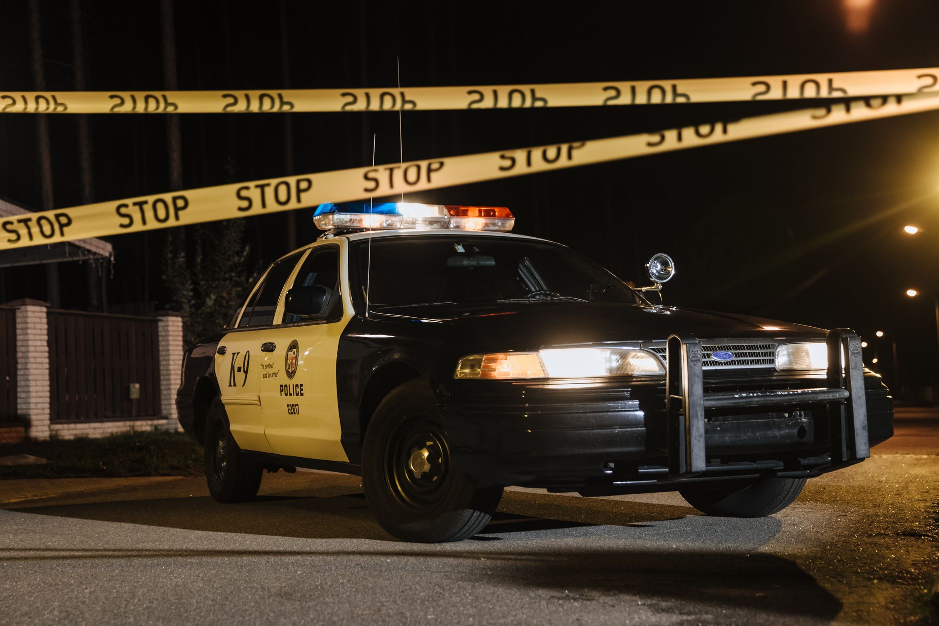 A police car parked at a night scene with yellow barricade tape, illuminated by streetlights