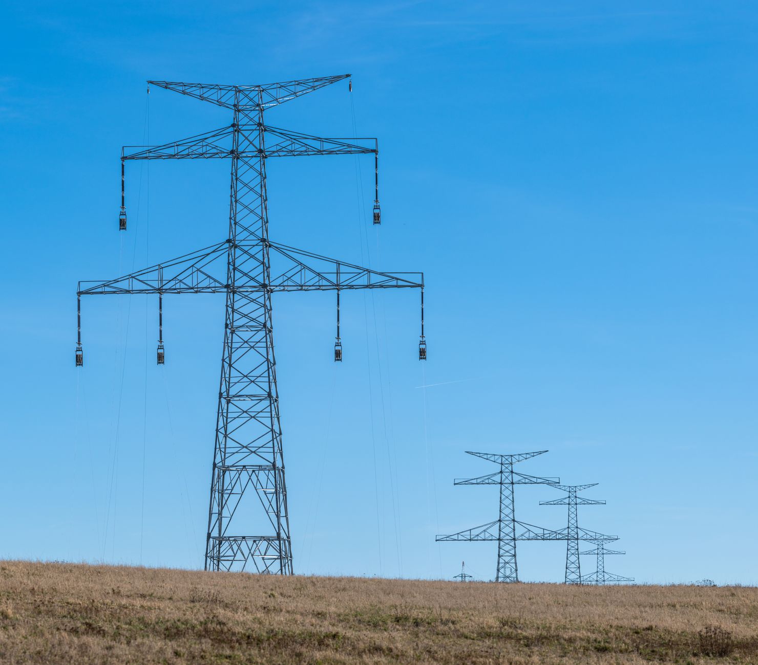 Electricity transmission towers against a blue sky over open countryside