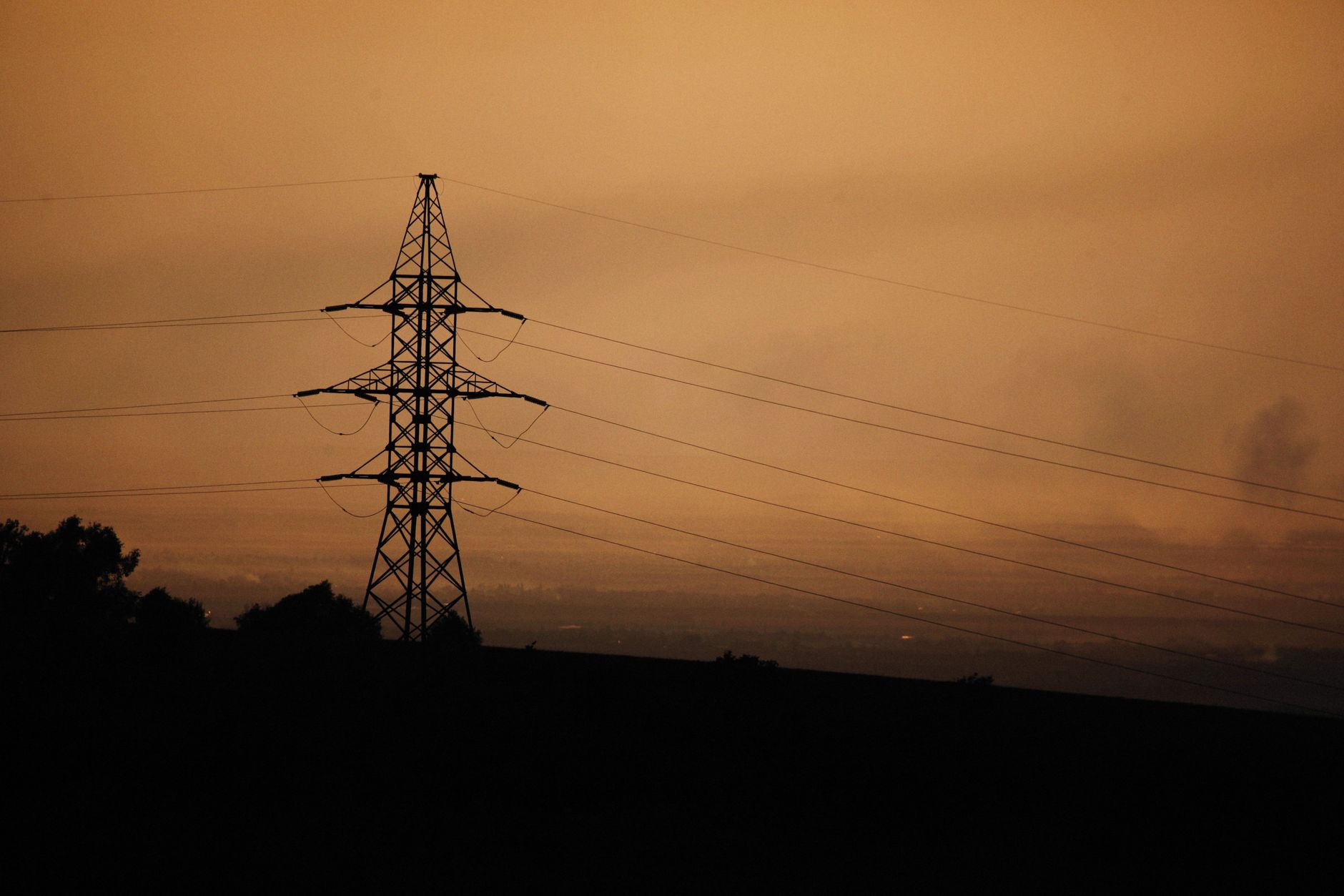 A power transmission tower silhouetted against a warm sunset sky