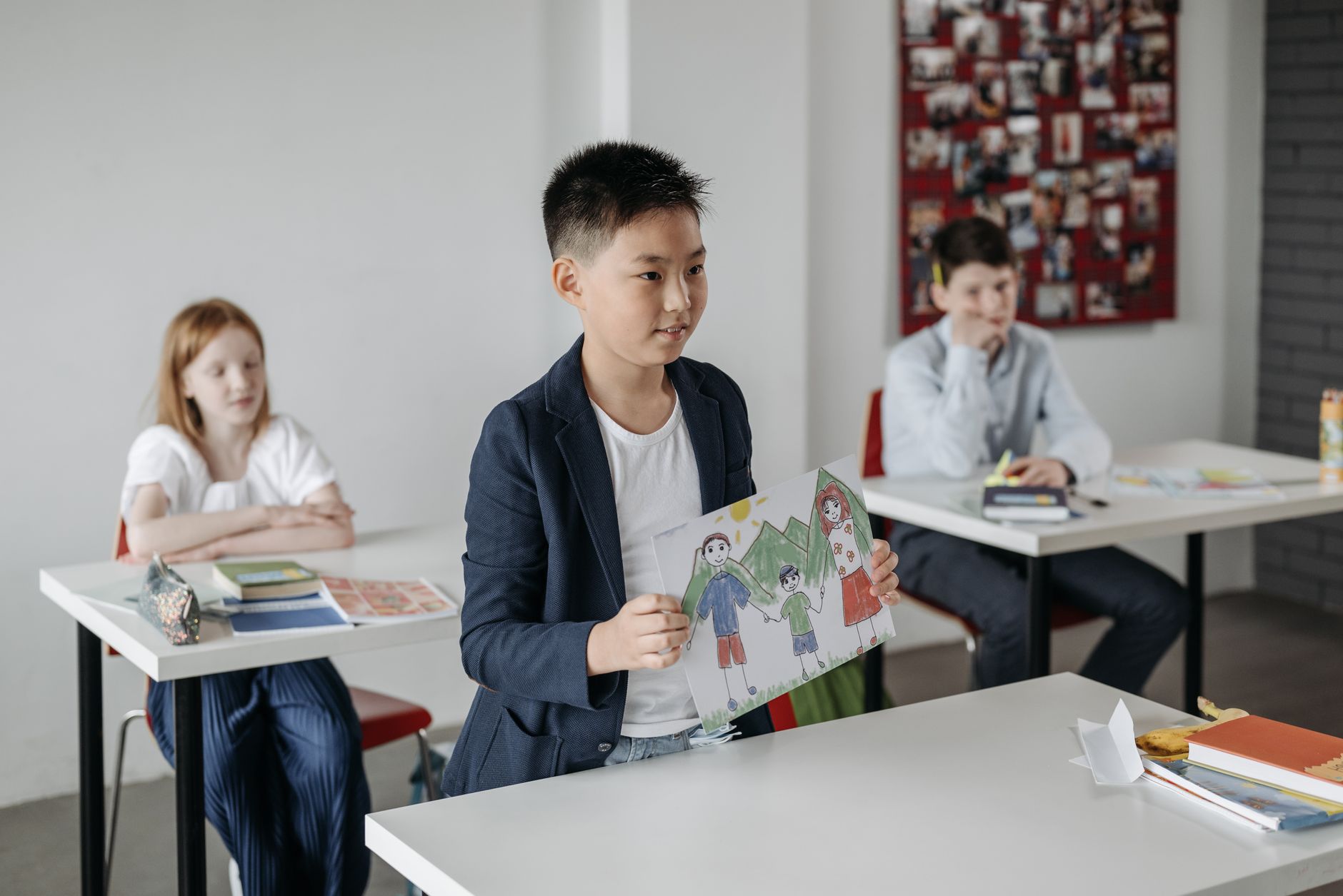 A child in a classroom holding up a drawing