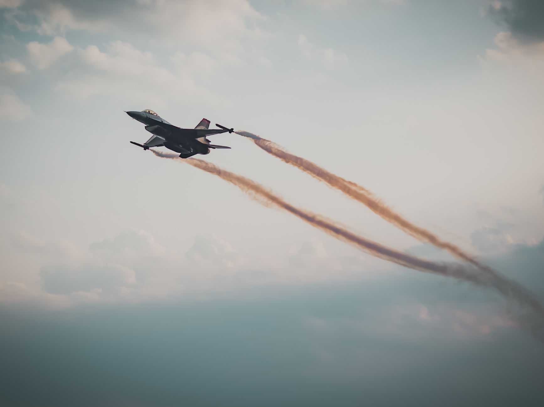 A military fighter jet flying through a cloudy sky