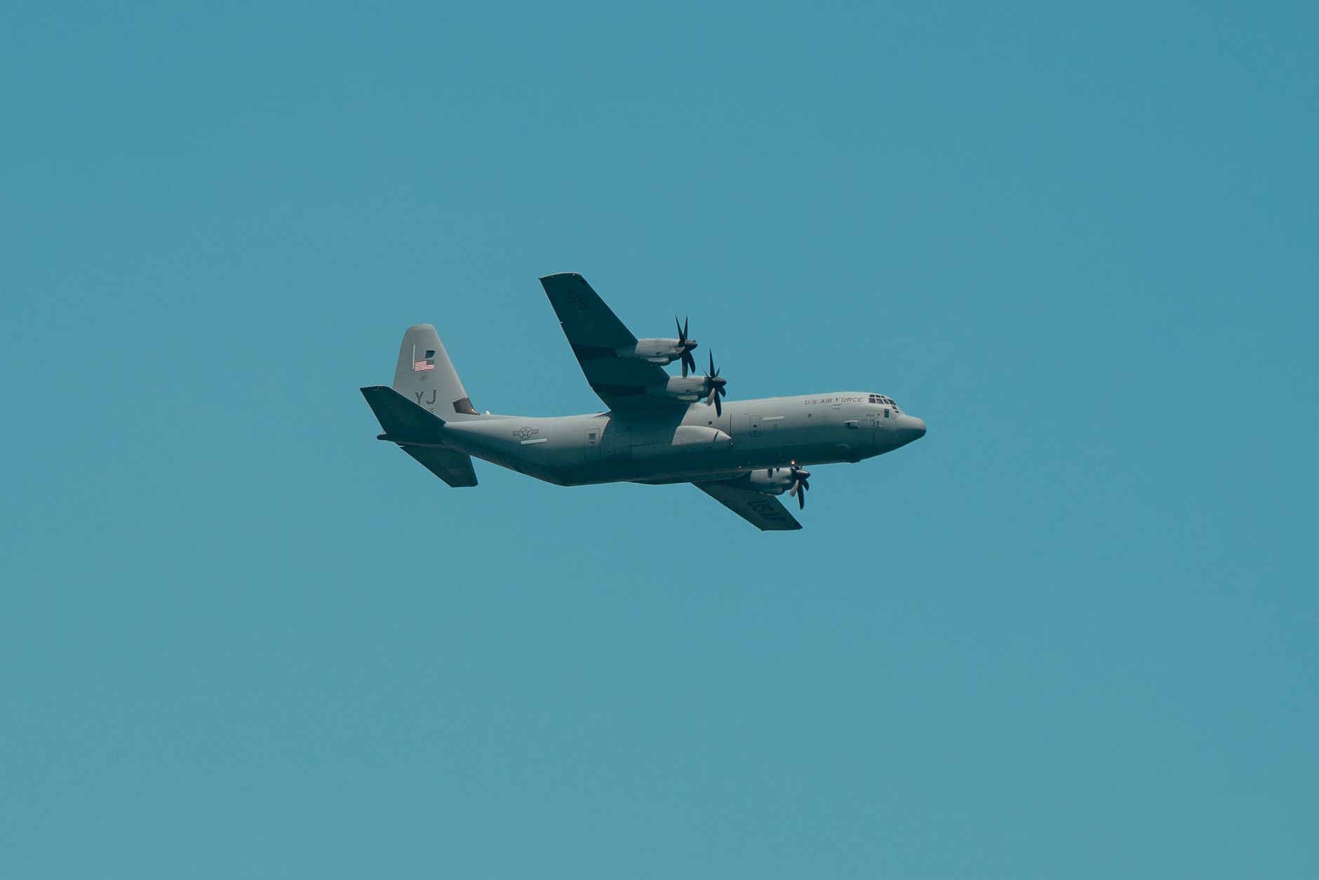 A military aircraft flying overhead against a clear blue sky