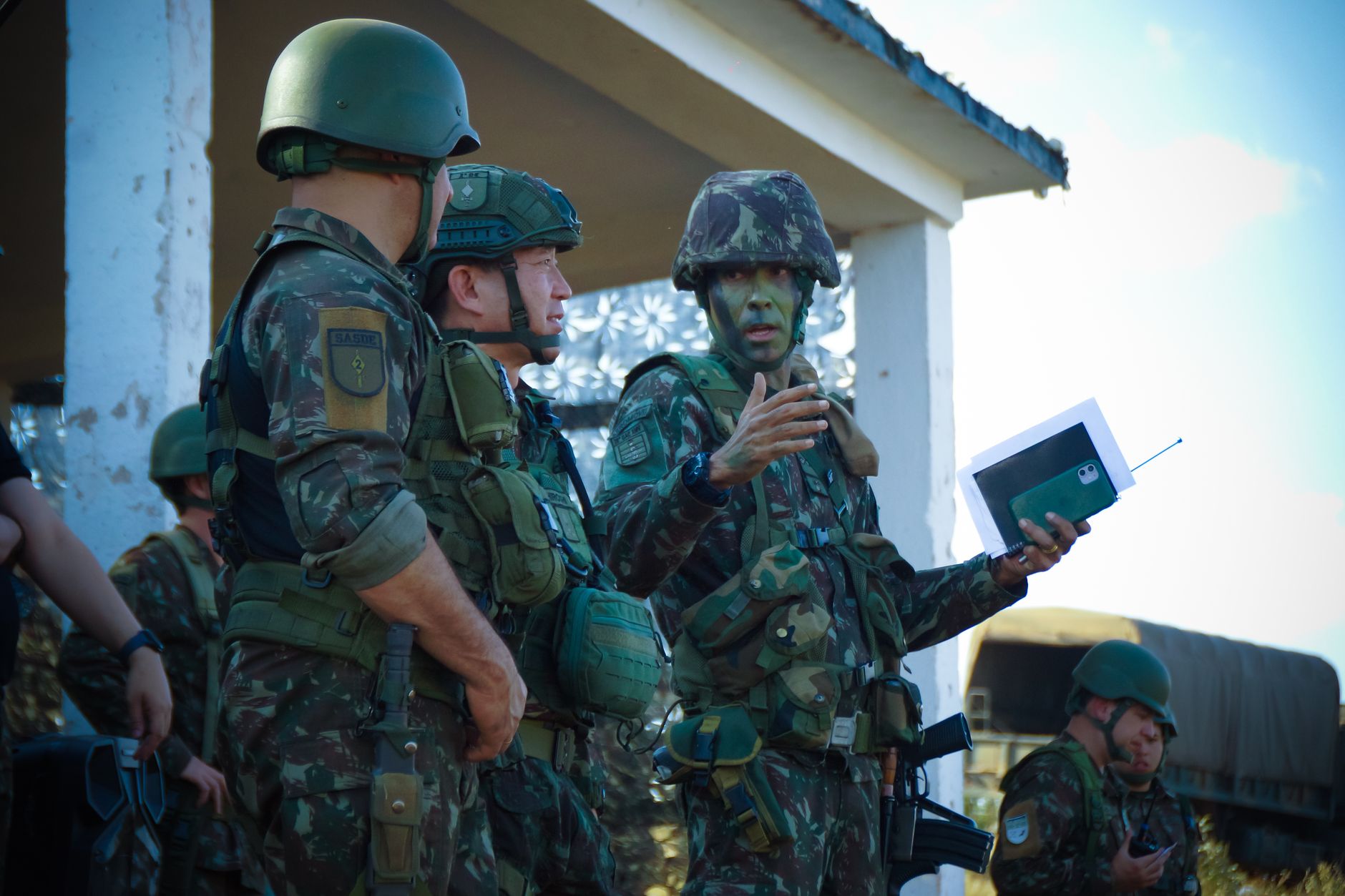 Soldiers in camouflage and tactical gear gathered for a military briefing outdoors
