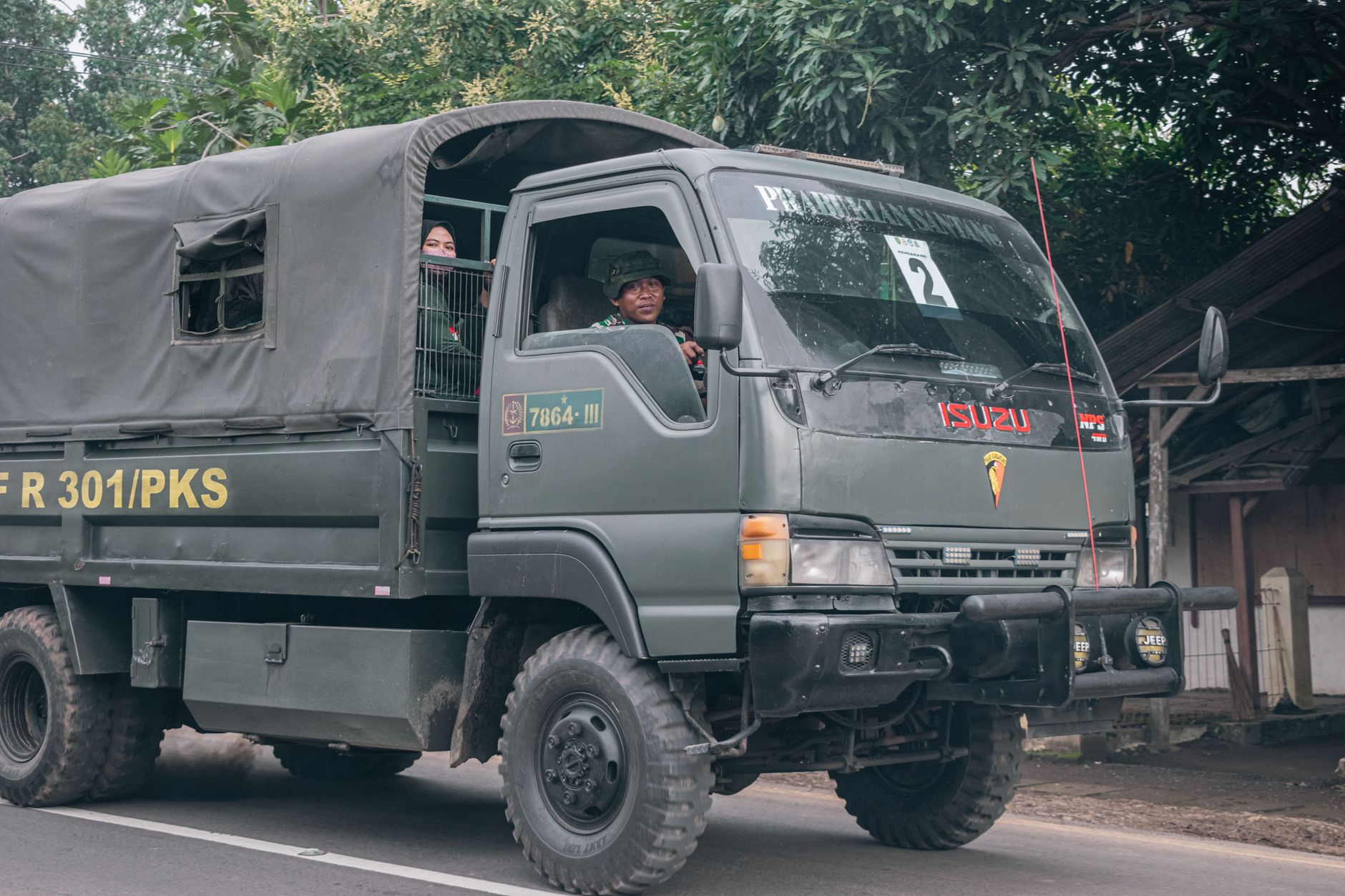 A military truck carrying soldiers drives along a rural road