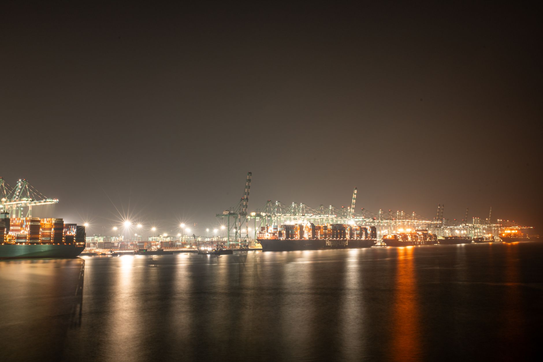Cargo ships and stacked shipping containers at a busy commercial port at night