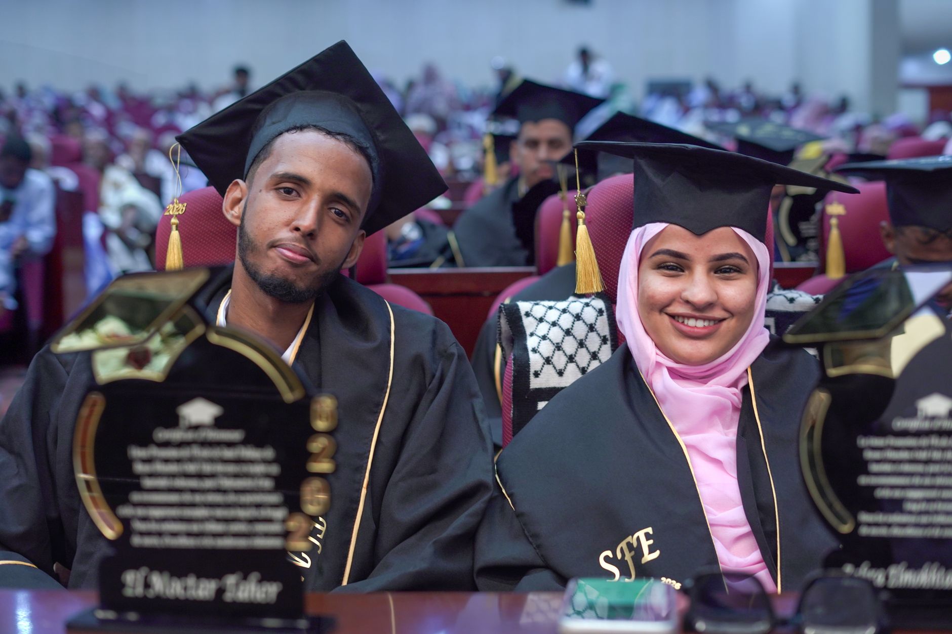 Two graduates in caps and gowns celebrating at a graduation ceremony
