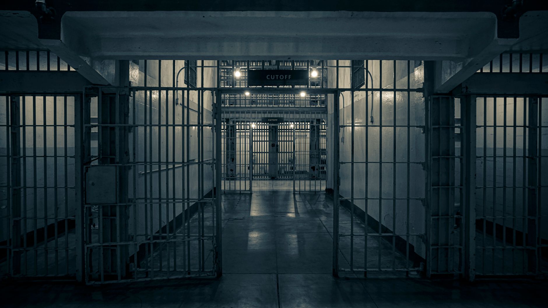 Moody interior of an empty prison corridor lined with metal bars