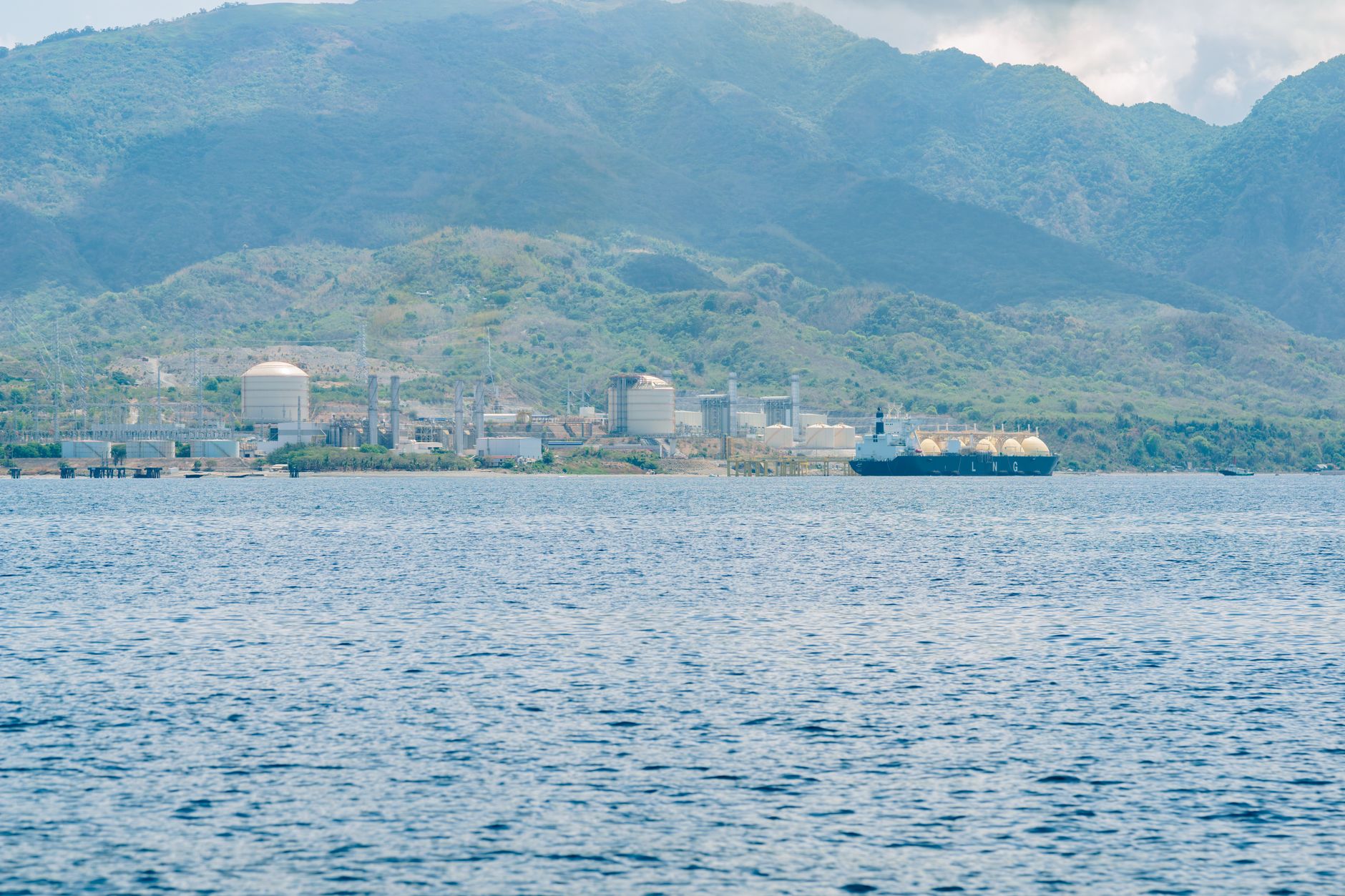 Industrial coastal facility with a docked LNG tanker against a mountain backdrop
