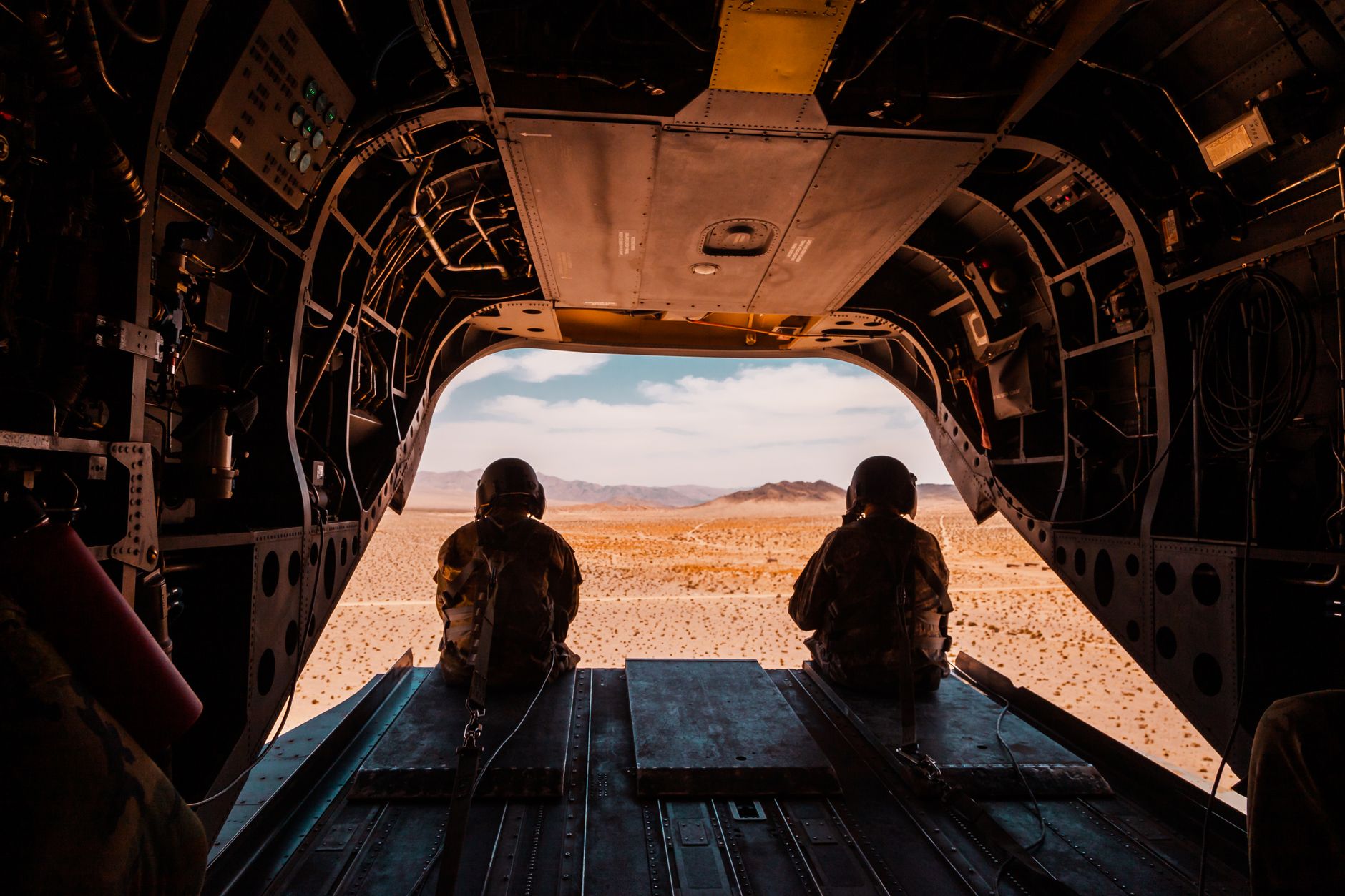 Soldiers seated in a military aircraft looking out over a desert landscape