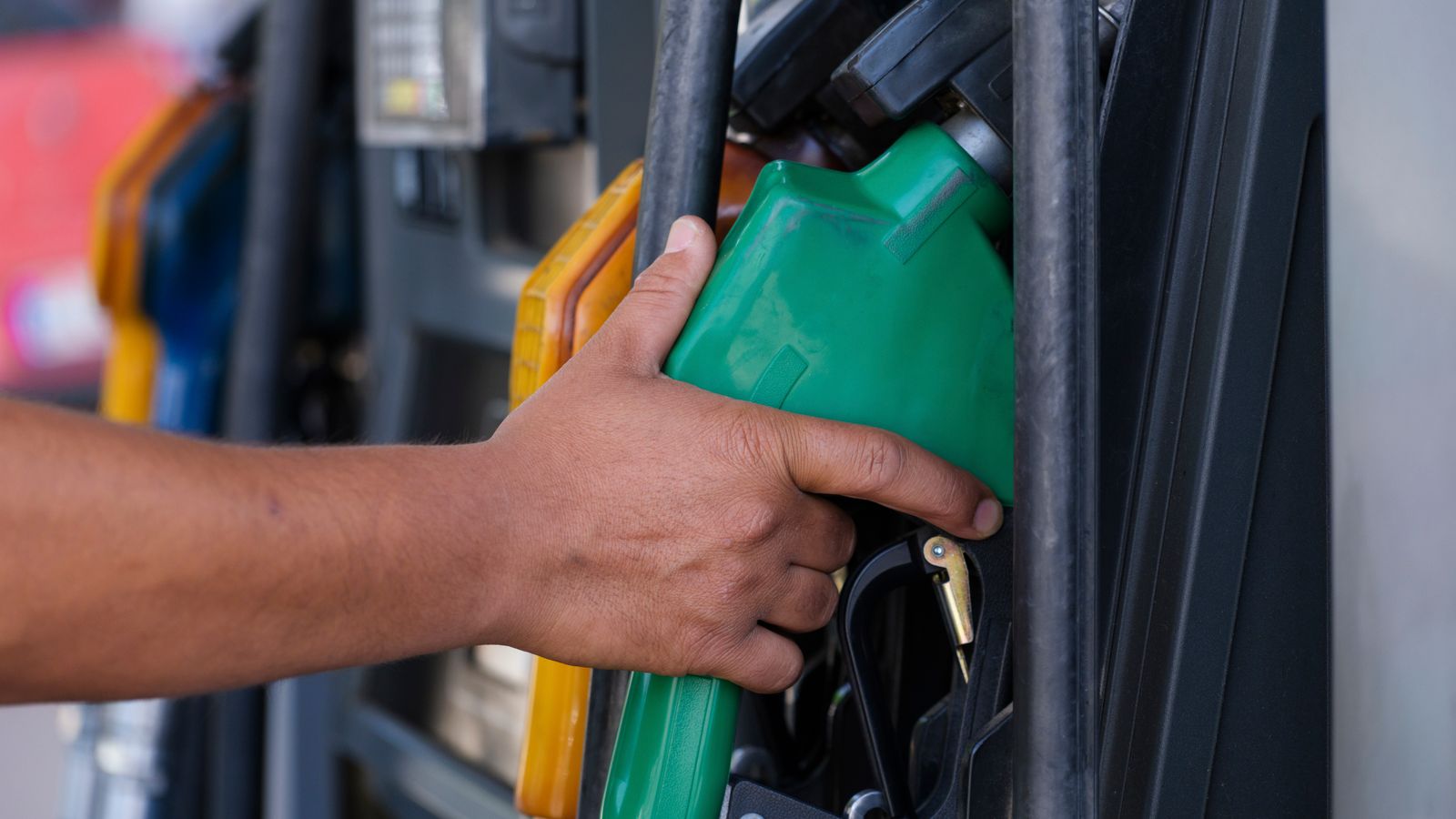 Close-up of a hand holding a green fuel pump nozzle at a filling station