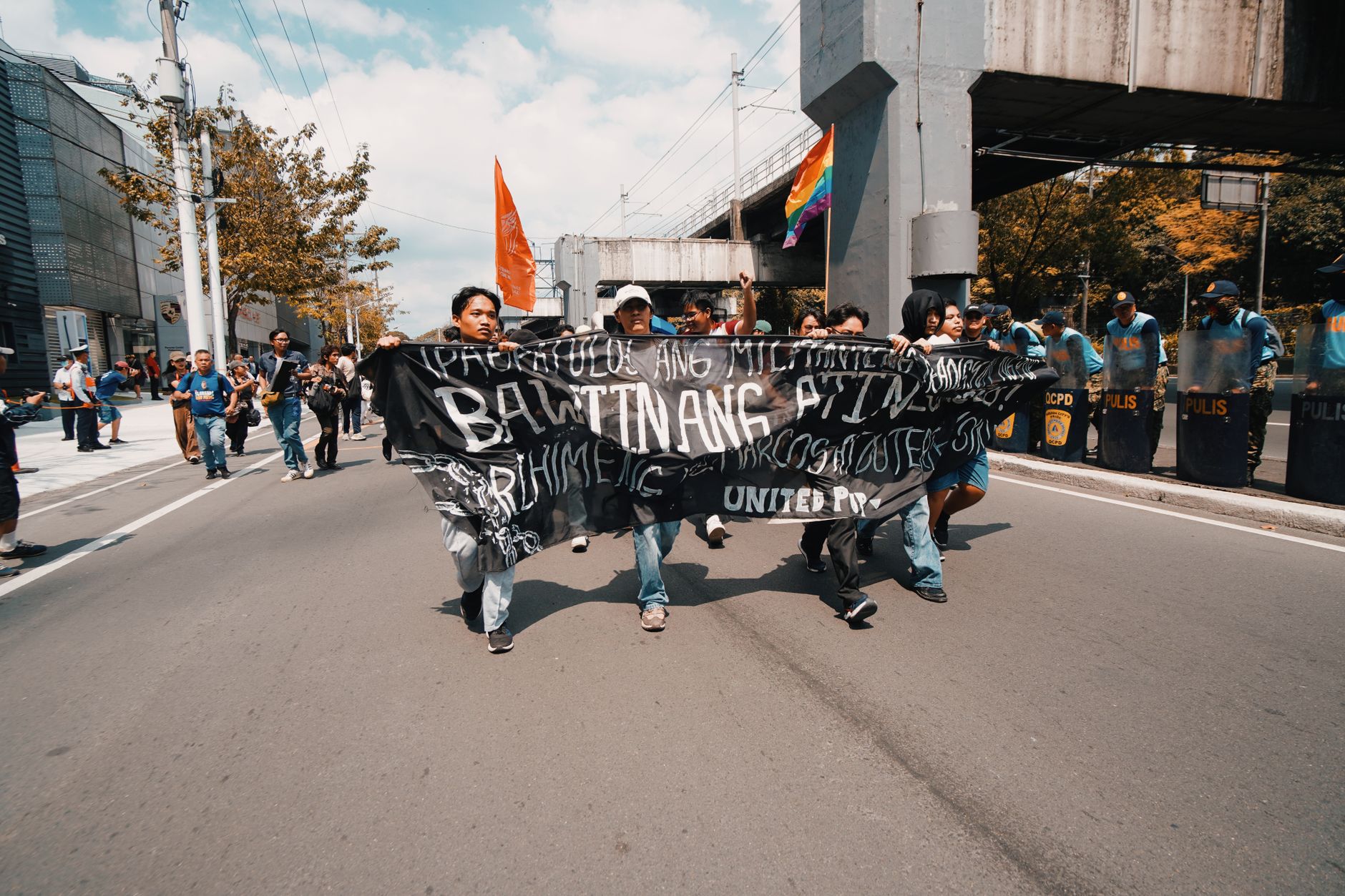 Protesters carrying a banner down a city street with police and flags in the background
