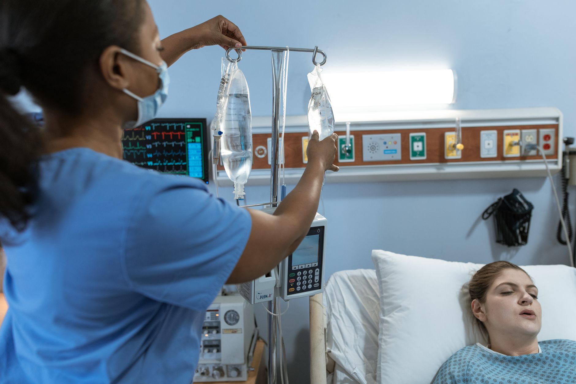 A nurse in a hospital setting adjusts an IV drip for a patient lying in bed
