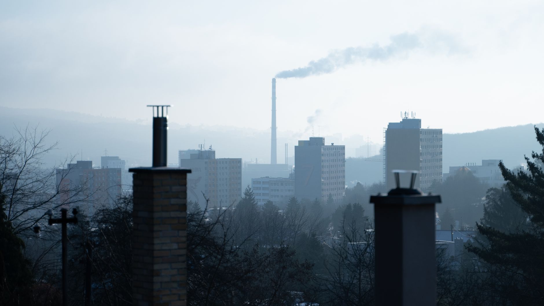 An urban landscape with chimneys, smoke, and tall buildings on a foggy, hazy day