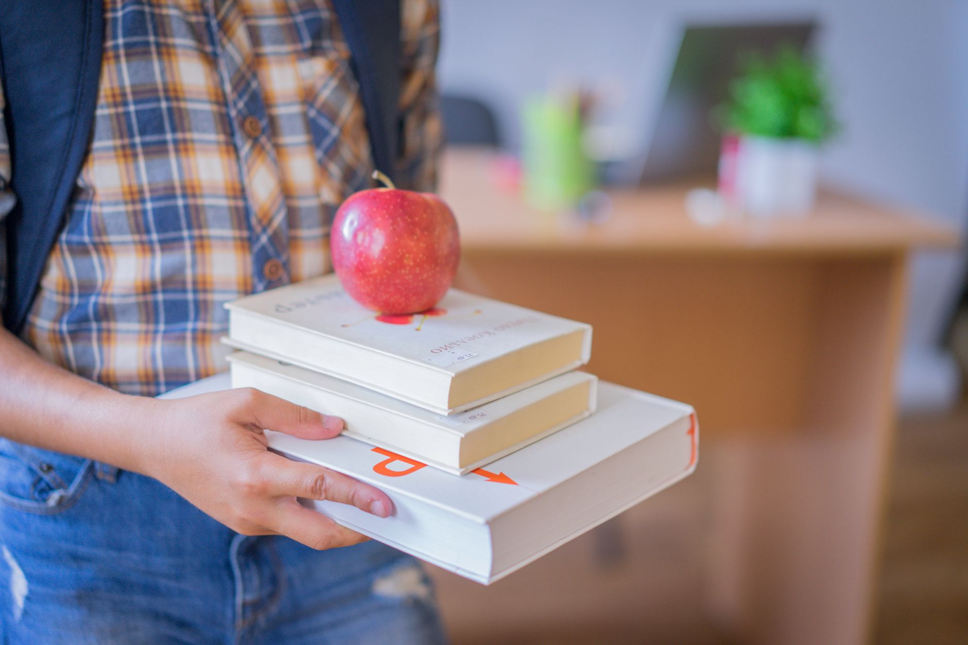 A child holding a stack of books with an apple on top in a classroom