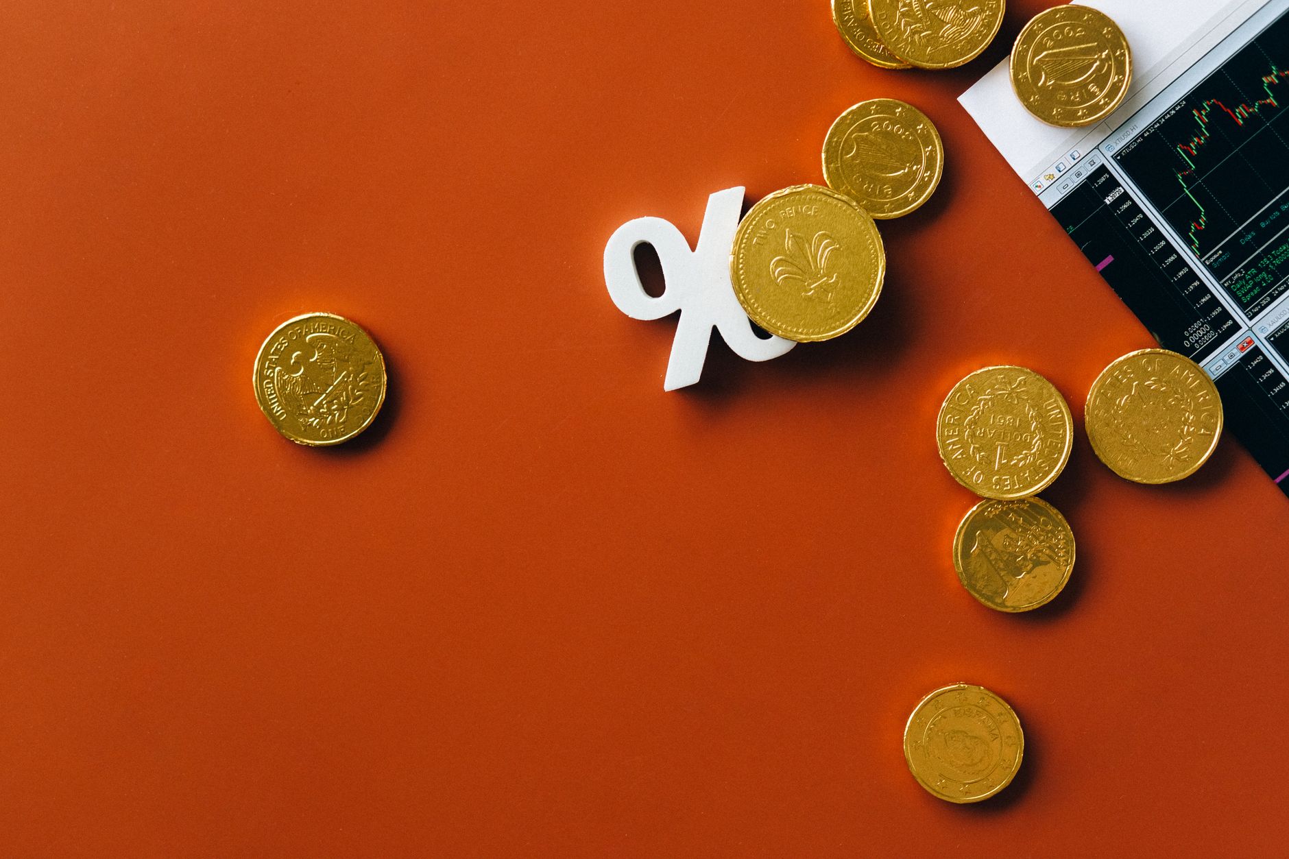 Gold coins scattered with a stock market graph and a percentage symbol on an orange background