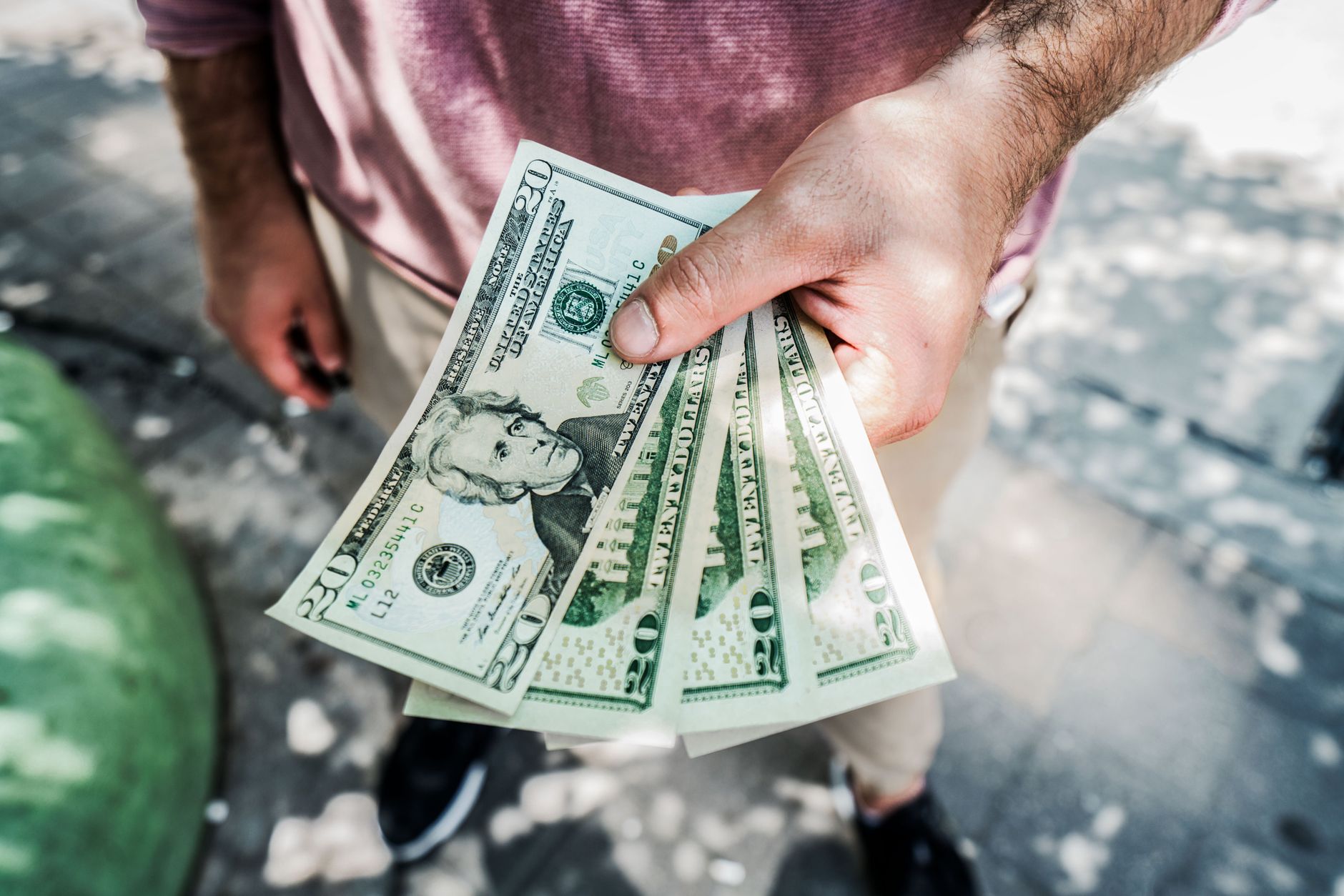 A person holding several twenty-dollar bills outdoors, depicting a payment or financial transaction