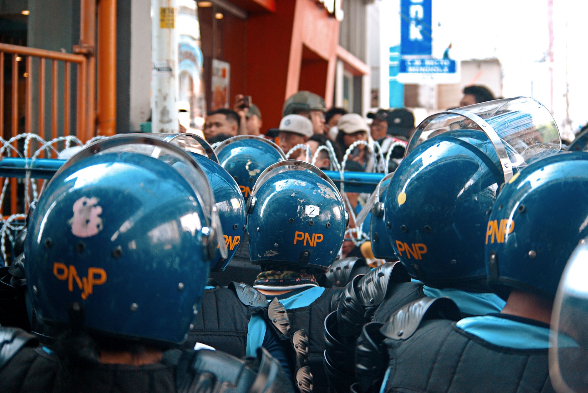Riot police officers in protective gear standing before a barbed wire barricade