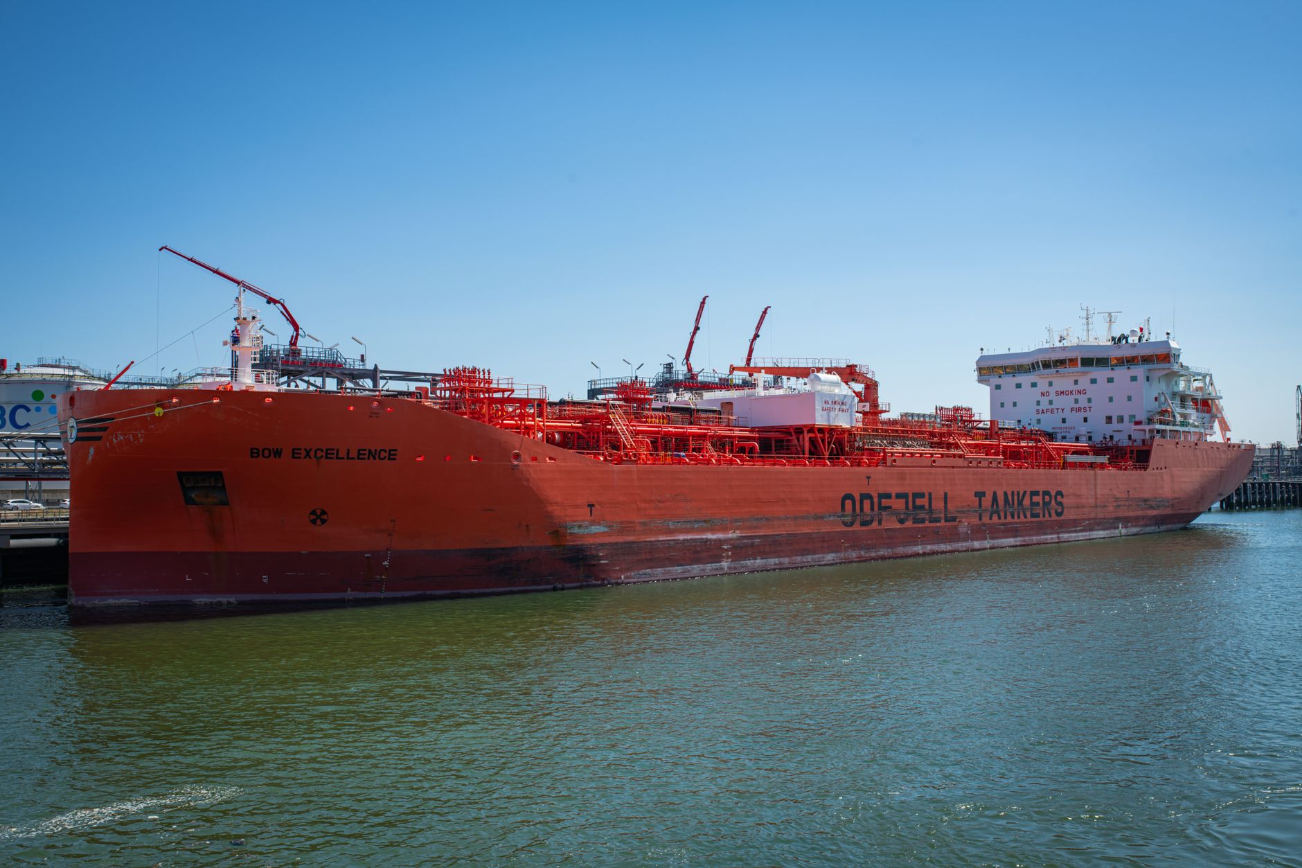 A large red oil tanker docked at a harbour under clear skies