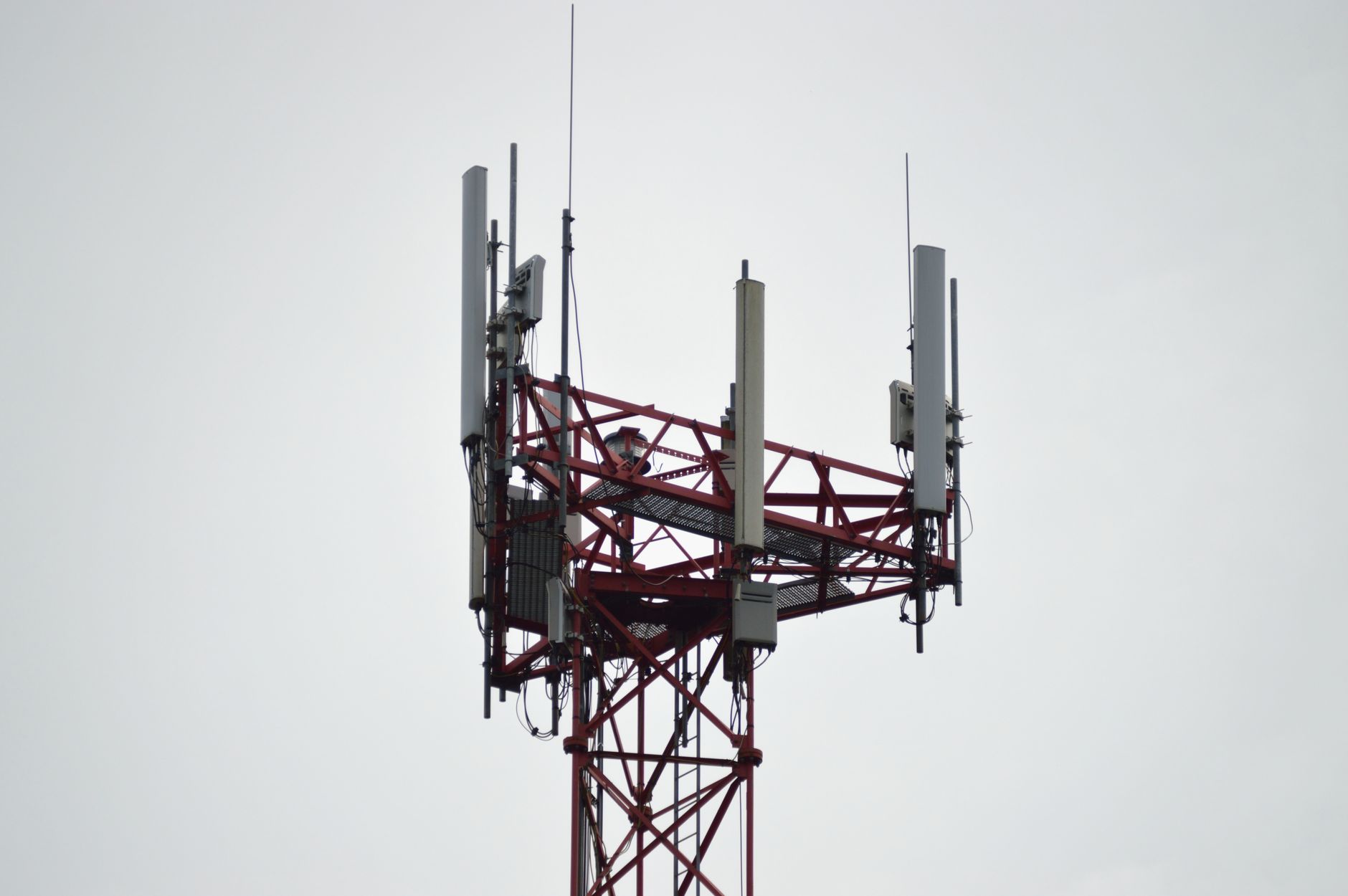 A red telecommunications signal tower with antennas against a grey sky